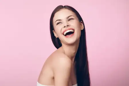 Смеющаяся молодая женщина с длинными волосами на розовом фоне