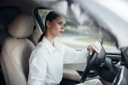 Женщина-водитель в салоне автомобиля держится за руль и смотрит в камеру: уверенная женщина сидит на водительском сиденье, положив руку на руль, и смотрит прямо в камеру с выражением спокойствия и