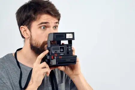 Фотограф-мужчина держит камеру с профессиональным объективом, творческая студийная работа, светлый фон