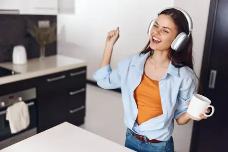 Женщина наслаждается моментом отдыха с кофе и музыкой на кухне, надев наушники