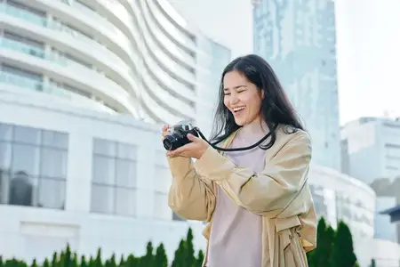 Женщина держит фотоаппарат в городской обстановке на открытом воздухе, с радостью и любопытством снимает горизонт и уличные детали