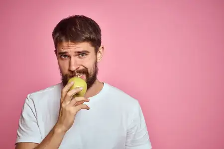 Милый мужчина с яблоком на розовом фоне, жестикулирует руками, белая футболка, свободное пространство