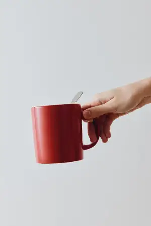 Красная кофейная кружка с ложкой, которую держит человек на белом фоне