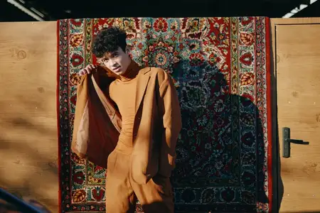 Модный мужчина-модель в теплом коричневом костюме уверенно стоит перед ярким, замысловатым ковром