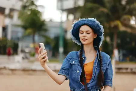 Молодая женщина держит смартфон и делает селфи в городском парке осенью