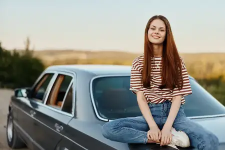 Молодая женщина сидит на багажнике автомобиля и отдыхает после трудной дороги, любуясь природой с красивым видом