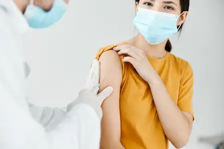 Врач делает инъекцию в плечо женщине в желтой футболке, крупный план