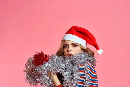 Женщина с мишурой на шее и в колпаке на голове на розовом фоне, обрезанный вид