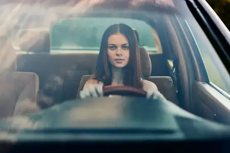 Молодая женщина с длинными волосами ведёт автомобиль, демонстрируя решимость и уверенность