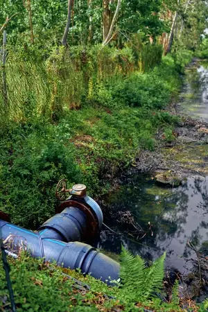 Заржавевшая труба и вентиль пропускают загрязненную воду в лесистый ручей
