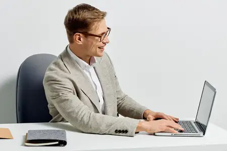 Улыбающийся мужчина в повседневном свитере работает за ноутбуком, сидя за белым столом