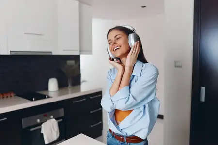 Женщина слушает музыку, стоя перед кухонной стойкой в интерьере дома