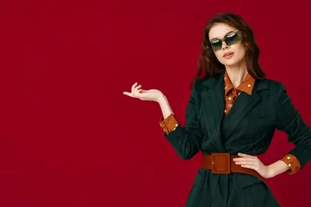 Красивая женщина в деловом костюме и солнцезащитных очках делает жест руками на изолированном фоне в студии