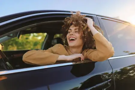 Яркая сцена с улыбающейся женщиной в автомобиле, наслаждающейся отдыхом на природе во время путешествия, с акцентом на образ жизни и ретро-цвет плёнки с золотистым светом и ностальгическими тонами…