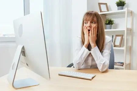 Взволнованная, расстроенная, очаровательная светловолосая бизнесвумен касается подбородка обеими руками, размышляя над решением проблемы в современном офисе