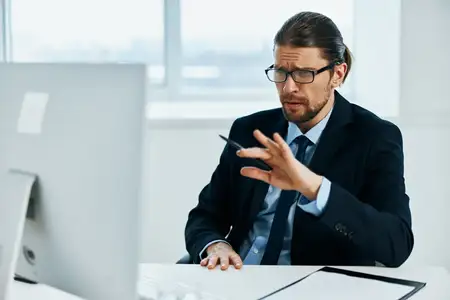 Офисный работник в очках излучает самоуверенность, работая за компьютером