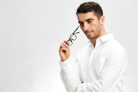 Мужчина в белой рубашке и очках с задумчивым взглядом, излучающий уверенность в себе