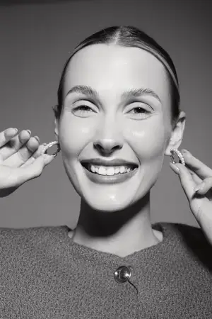 Крупноплановый портрет счастливой светлокожей женщины европеоидной расы, которая держит серьги у лица и тепло улыбается при студийном свете