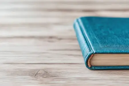 Детальный снимок книги в бирюзовом твёрдом переплёте на деревянной поверхности, передающий ощущение знаний и творчества