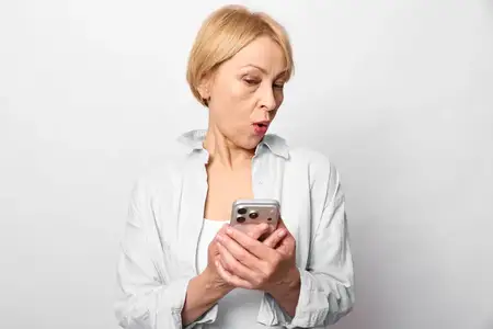 Удивленная женщина держит смартфон, выглядя обеспокоенной и встревоженной во время проверки сообщения