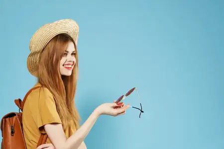 Женщина в шляпе, модной одежде, с рюкзаком, веселая, на синем фоне, улыбается