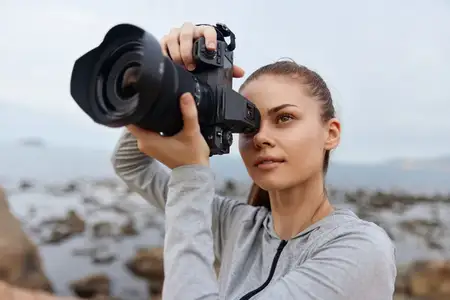 Решительная молодая женщина-фотограф делает потрясающие снимки природы своей зеркальной камерой у моря