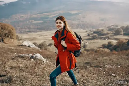 Путешественник в куртке, джинсах и ботинках поднимается в горы на фоне природного ландшафта