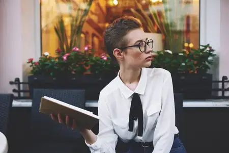 Женщина с короткой стрижкой стоит на улице с книгой в руках
