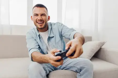 Увлеченный мужчина с улыбкой играет в видеоигры на уютном диване, что отражает современное сочетание развлечений и психического благополучия