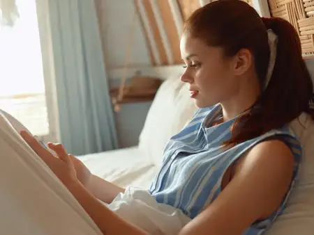 Женщина в удобной домашней одежде лежит на кровати, печатая сообщение на мобильном телефоне, что передает момент расслабления дома
