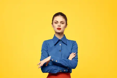 Привлекательная женщина в голубой рубашке жестикулирует руками, красная юбка, жёлтый фон, портрет, обрезанный вид