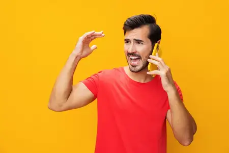 Мужчина в очках улыбается, показывая зубы, и указывает на что-то, держа смартфон