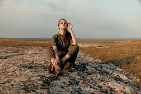Женщина курит сигарету на вершине скалы посреди поля во время поездки на природу