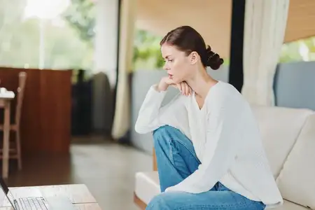 Улыбающаяся женщина использует ноутбук на диване в домашнем офисе для онлайн-обучения и общения