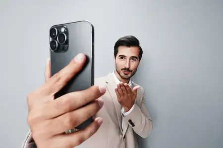Мужчина в деловом костюме с бородой улыбается и делает селфи на смартфон во время звонка