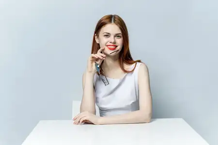 Женщина в белом платье сидит за столом, в руках бокалы, её шарм подчёркивают красные губы