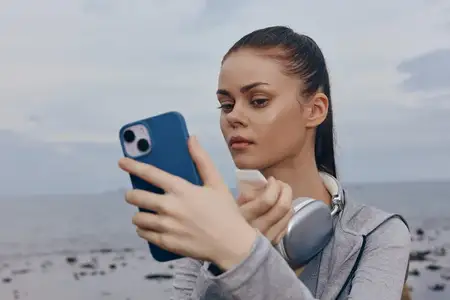 Молодая женщина в спортивной одежде проверяет свой смартфон у океана, демонстрируя сосредоточенность и преданность здоровому образу жизни на фоне спокойного пейзажа