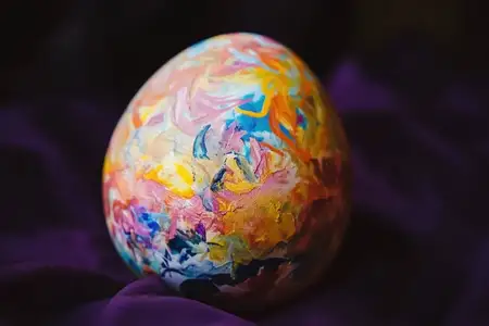 Потрясающее красочное пасхальное яйцо ручной росписи с уникальным дизайном лежит на богатом фиолетовом тканевом фоне, символизируя весенние праздники, творчество и торжество