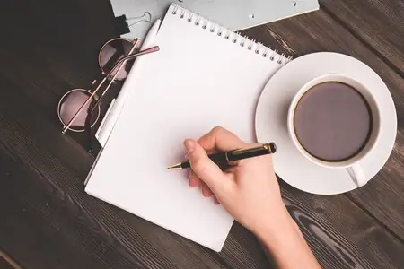 Записная книжка с ручкой на деревянном столе, чашка кофе