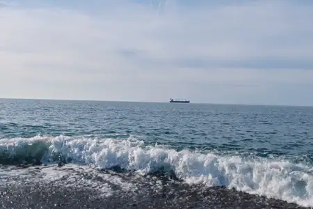 Прибрежный морской пейзаж: голубая вода и накатывающие волны у берега, одинокое судно на горизонте, яркое небо и безмятежная атмосфера над морем