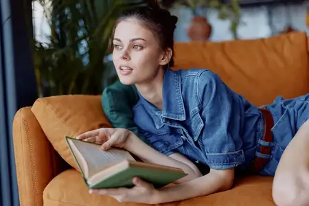 Женщина расслабляется дома, читая книгу на диване