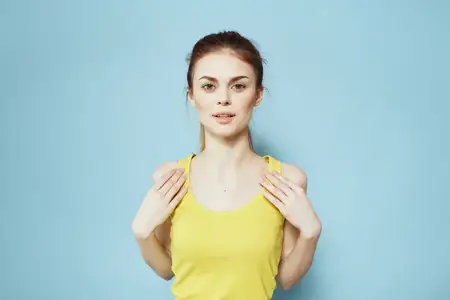 Спортивная женщина в жёлтом топе на лямках и с хвостиками на голове занимается фитнесом на синем фоне