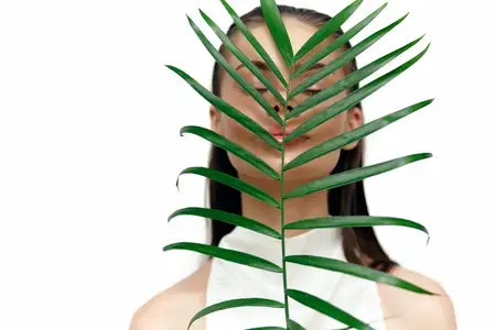 Изящная модель, частично скрытая пышной зеленой пальмовой ветвью, вызывает чувство умиротворения и элегантности
