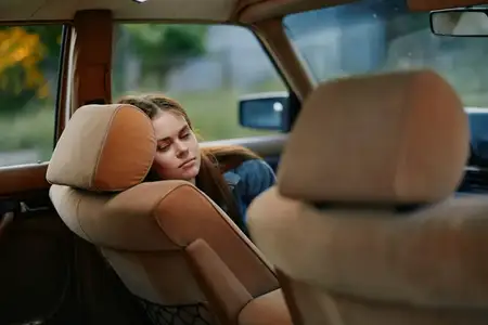 Безмятежная молодая женщина с длинными каштановыми волосами, отдыхающая на сиденье винтажного автомобиля, запечатлевающая момент спокойствия в солнечной обстановке на открытом воздухе
