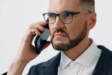 Портрет передает лидерство и экспертизу, когда он говорит по ручному телефону, с твердыми бровями и сомкнутыми губами, демонстрируя решимость и вовлеченность на чистом цветном фоне