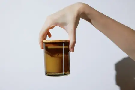 Рука держит стеклянную банку с коричневой жидкостью на белом фоне
