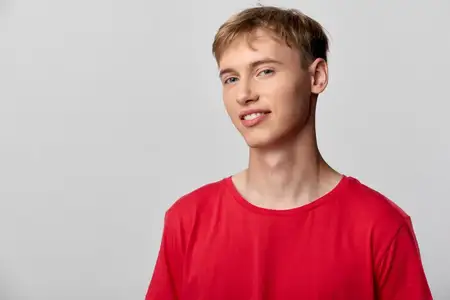 Мужчина-модель в повседневной красной футболке позирует в минималистичной студии