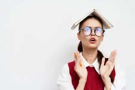 Молодая женщина в очках с удивленным выражением лица балансирует книгой на голове, символизируя творческое мышление и мозговой штурм