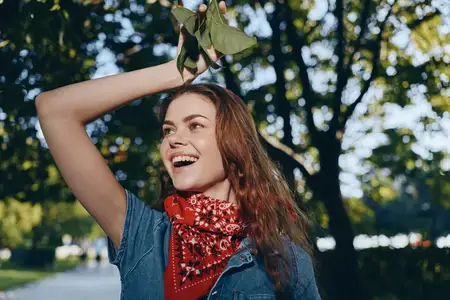 Радостная женщина в стиле life-style, одетая в современную джинсовую куртку в стиле бохо-вестерн и красную бандану, в залитом солнцем парке, воплощая повседневный уличный стиль с плёночным цветом