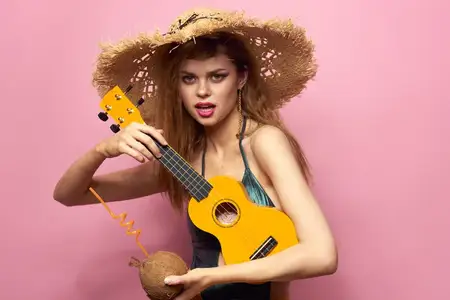 Женщина держит укулеле, кокосовый коктейль и соломенную шляпу на пляже